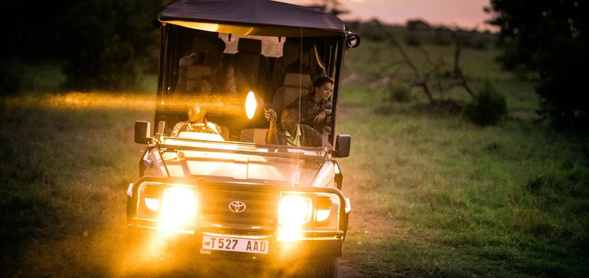 Grumeti Hills safari vehicle with headlights on at dusk, setting out on a night drive