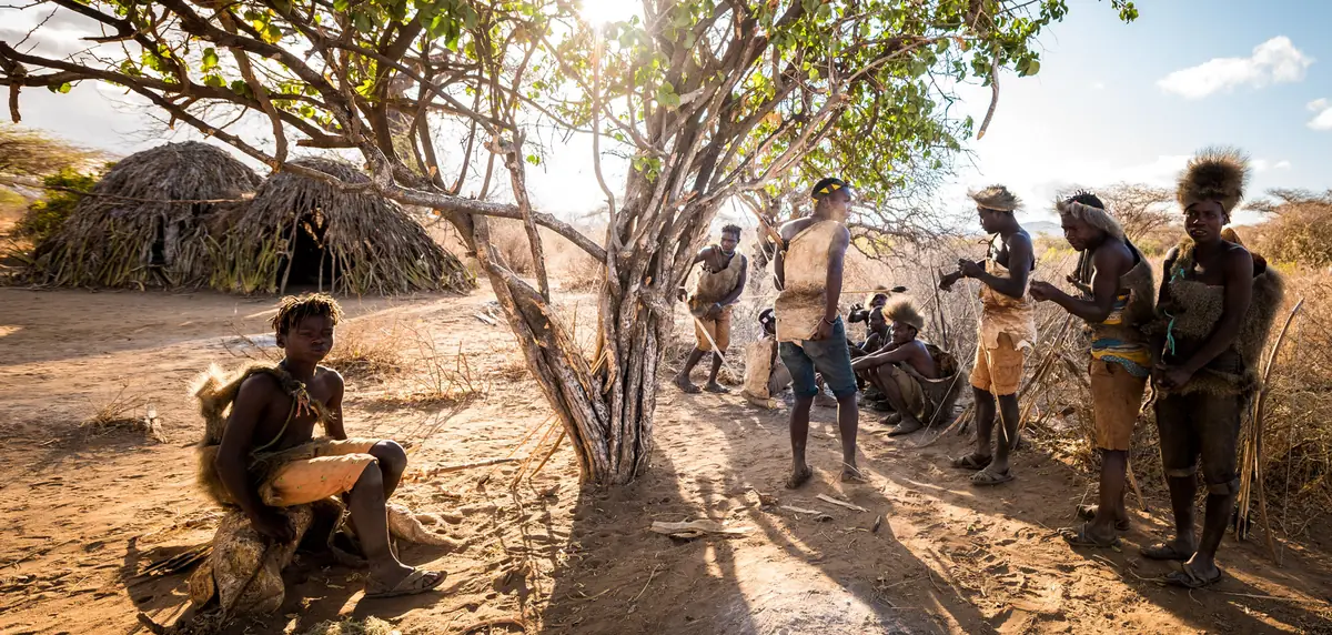 Hadzabe men gathered by their grass huts near Lake Eyasi