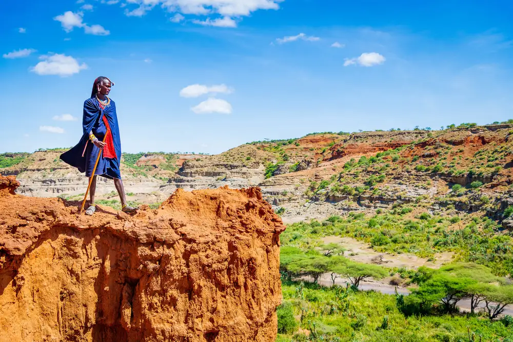 A Maasai guide standing on the eroded edge of Olduvai Gorge above the green valley floor