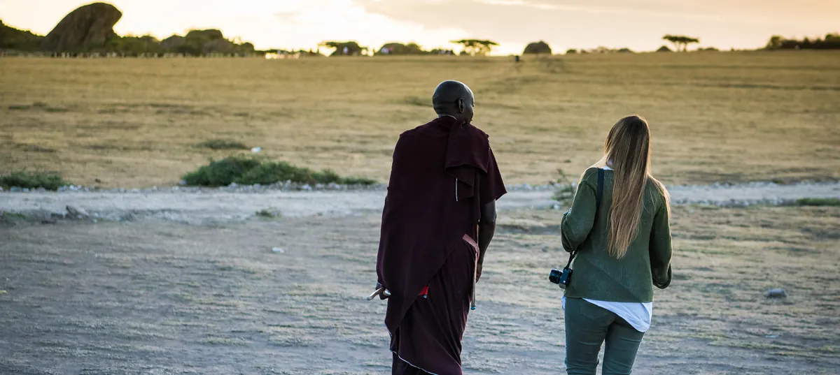 A Maasai host walking with a guest across the plain on a village visit