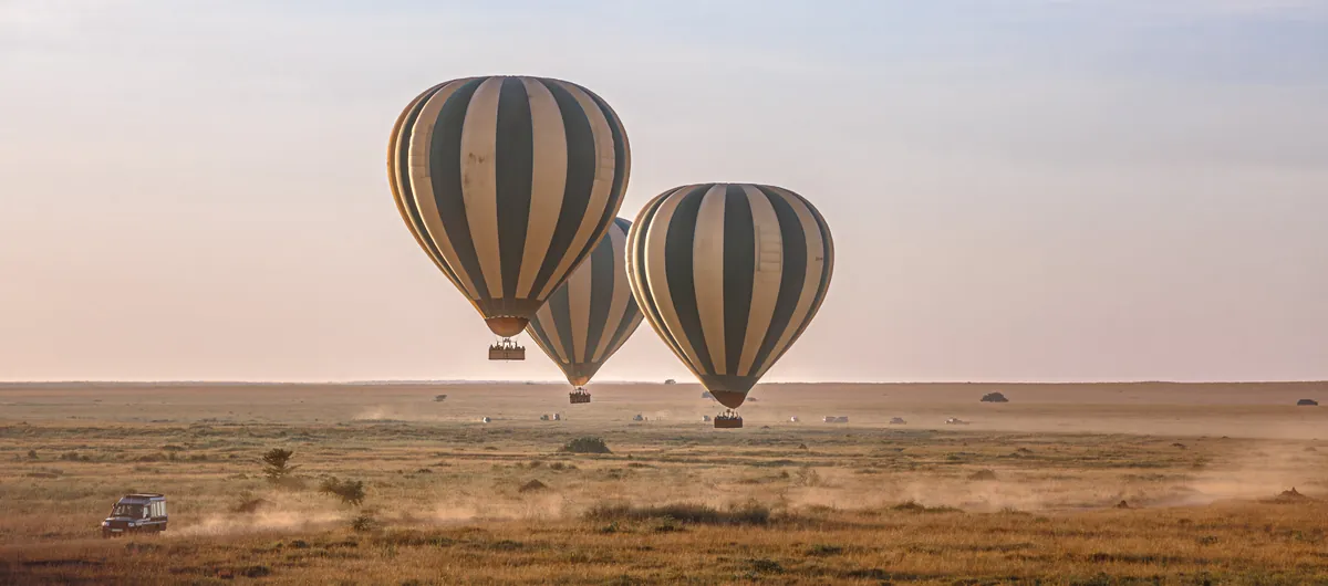 Two hot air balloons drifting low over the central Serengeti plains at dawn